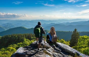 A hikincouple relaxing on the rock with a view of mountains and a valley